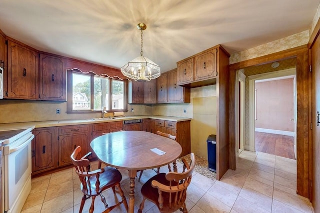 kitchen featuring white appliances, a sink, hanging light fixtures, light countertops, and brown cabinets