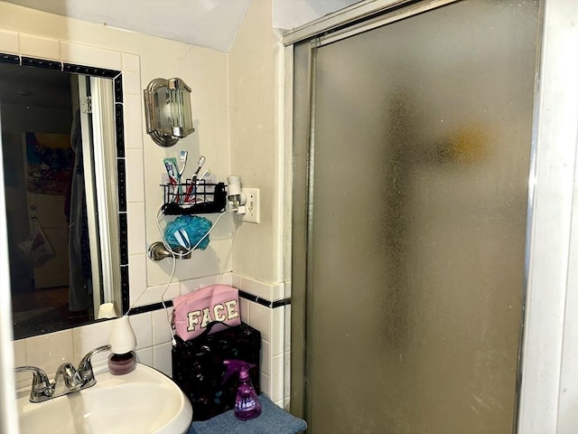 bathroom featuring a shower with door, sink, tile walls, and decorative backsplash