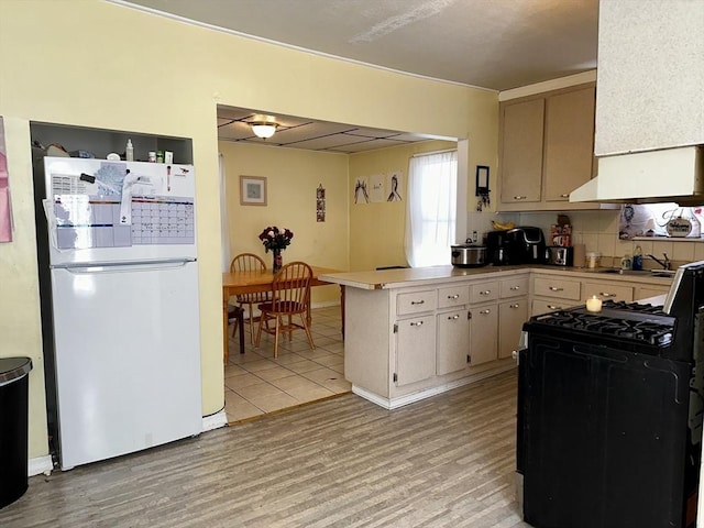 kitchen featuring sink, light hardwood / wood-style flooring, white refrigerator, gas range oven, and kitchen peninsula