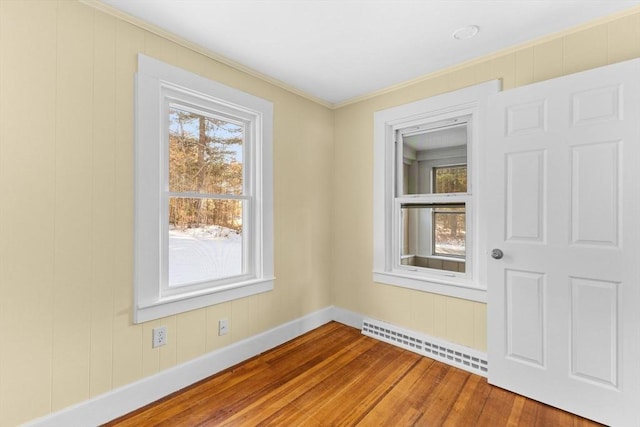 unfurnished room featuring hardwood / wood-style flooring, a baseboard radiator, and crown molding