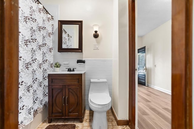 bathroom with toilet, wood finished floors, vanity, baseboards, and tile walls