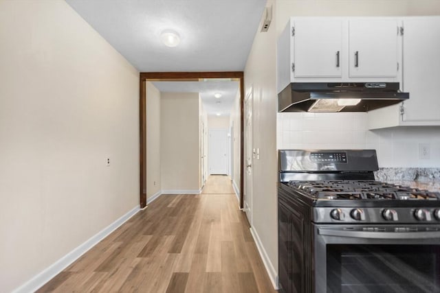 kitchen with light wood-style flooring, under cabinet range hood, white cabinetry, stainless steel gas range, and backsplash