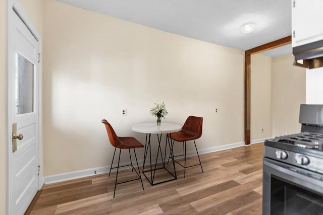 kitchen featuring light wood-type flooring, stainless steel gas range oven, baseboards, and white cabinets