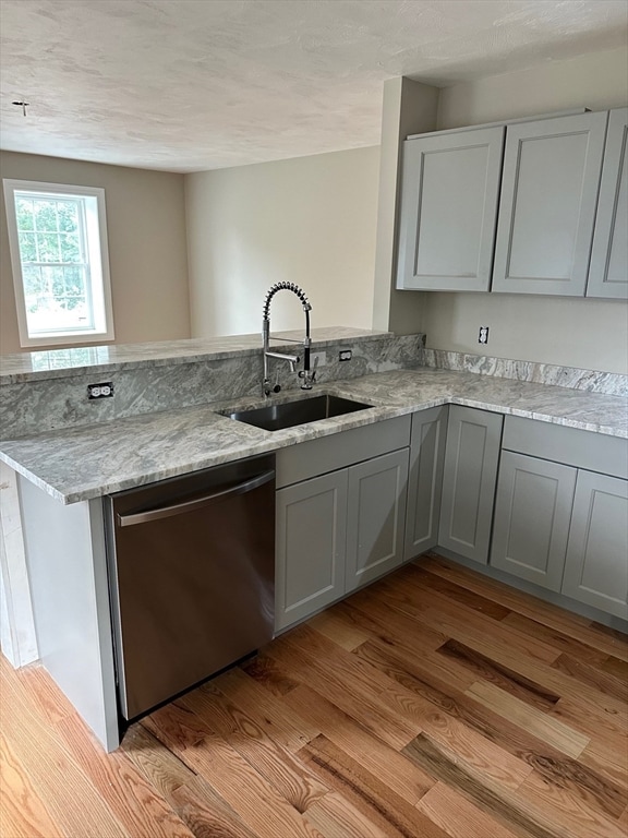 kitchen featuring sink, stainless steel dishwasher, light wood-type flooring, light stone counters, and kitchen peninsula