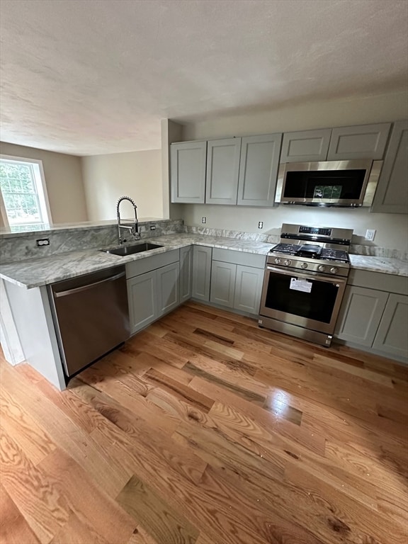 kitchen featuring gray cabinetry, sink, light stone counters, light hardwood / wood-style flooring, and appliances with stainless steel finishes