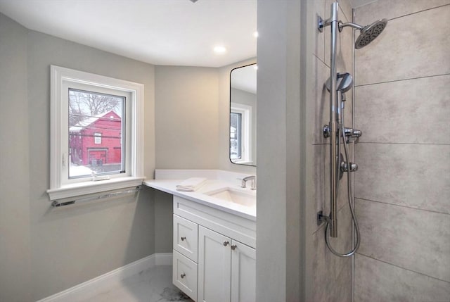 full bathroom with baseboards, tiled shower, and vanity