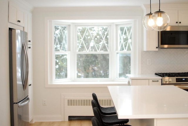 kitchen with crown molding, radiator, backsplash, appliances with stainless steel finishes, and white cabinets