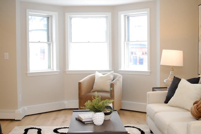 living room with a baseboard heating unit, a healthy amount of sunlight, baseboards, and wood finished floors