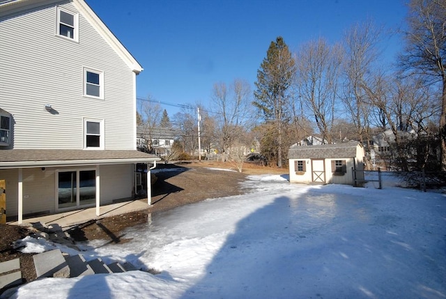 snowy yard featuring an outbuilding, a shed, and a patio area