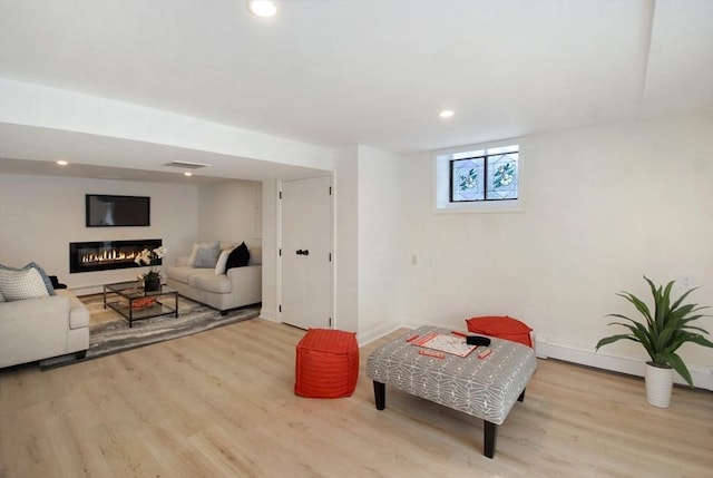 living area with a baseboard radiator, a glass covered fireplace, recessed lighting, and wood finished floors