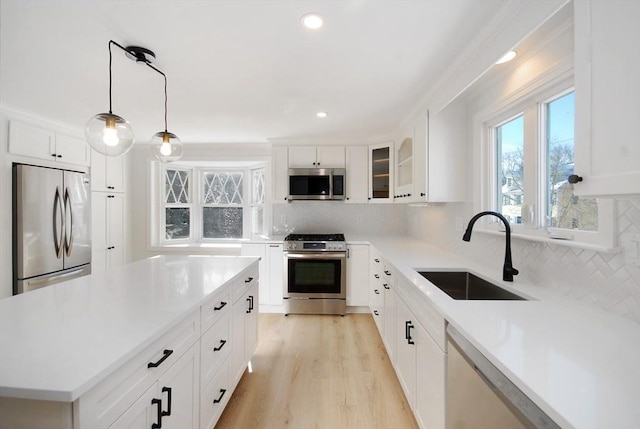 kitchen with light wood finished floors, decorative backsplash, appliances with stainless steel finishes, light countertops, and a sink