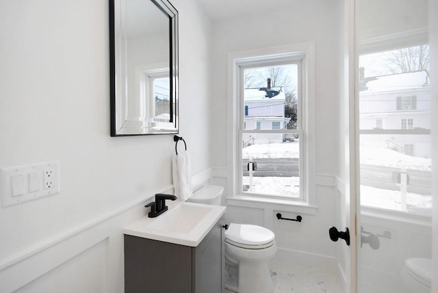 bathroom with a wealth of natural light, wainscoting, vanity, and toilet