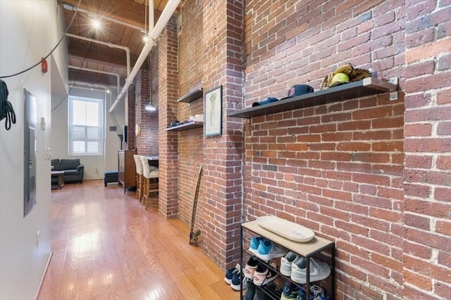 hallway with wood ceiling, hardwood / wood-style floors, vaulted ceiling with beams, and brick wall