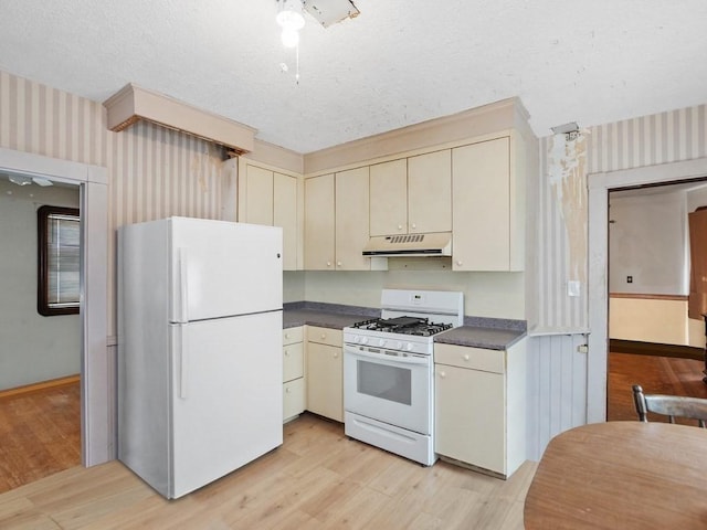 210-212 Brown St, Waltham, MA 02453 - kitchen with white appliances, cream cabinets, under cabinet range hood, wallpapered walls, and dark countertops