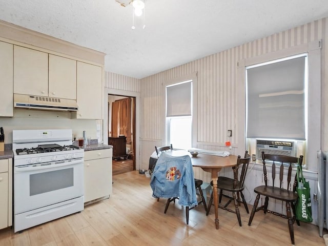 210-212 Brown St, Waltham, MA 02453 - kitchen featuring white gas range oven, under cabinet range hood, cream cabinetry, wallpapered walls, and light wood finished floors
