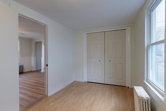 unfurnished bedroom featuring light hardwood / wood-style floors, radiator, and a closet