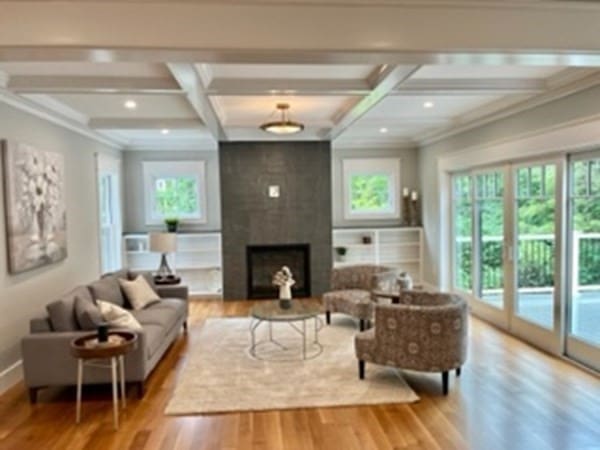 living room featuring light wood-type flooring, beam ceiling, a large fireplace, coffered ceiling, and crown molding