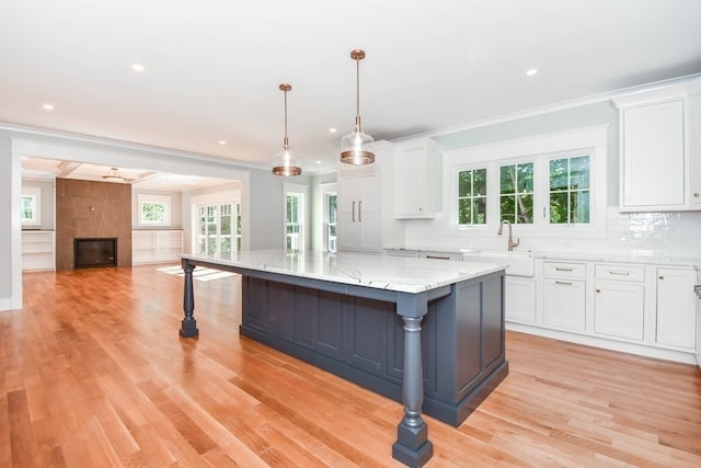 kitchen with a fireplace, a spacious island, decorative light fixtures, light hardwood / wood-style floors, and white cabinets