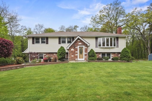 raised ranch featuring a chimney, a front lawn, and brick siding