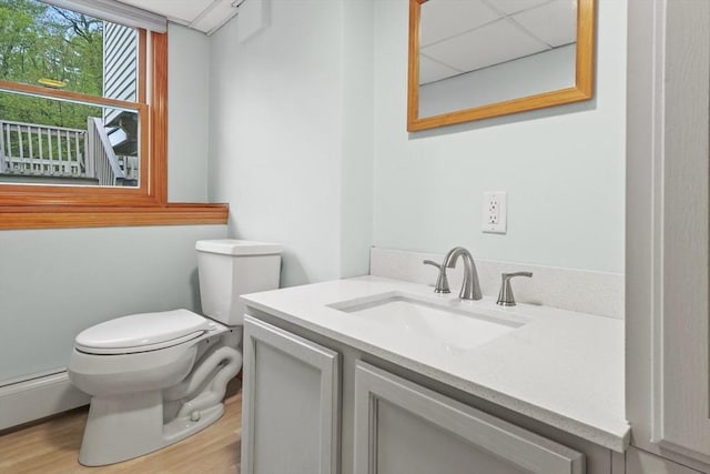 half bathroom with toilet, a baseboard radiator, wood finished floors, and vanity
