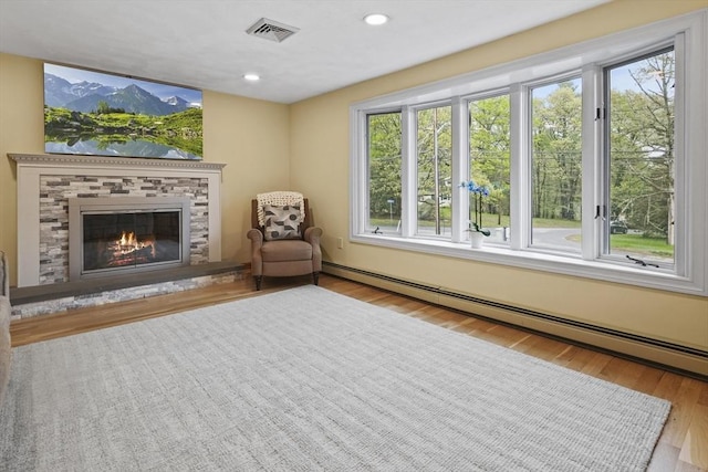 sitting room featuring a baseboard radiator, wood finished floors, a stone fireplace, and recessed lighting
