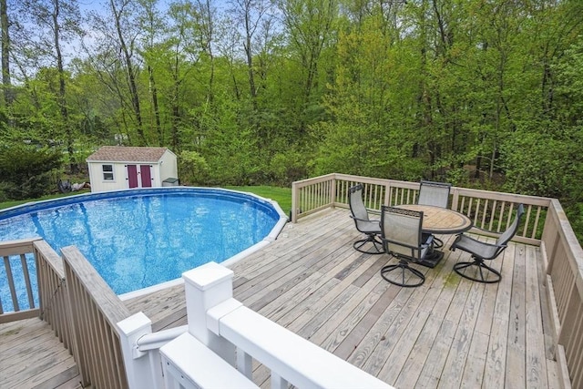 swimming pool with a deck, outdoor dining area, an outdoor structure, and a forest view