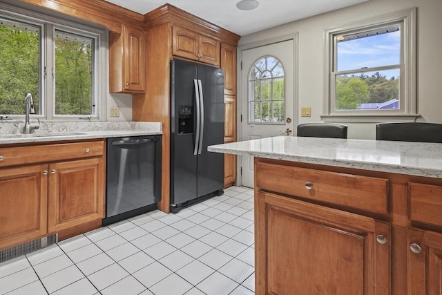 kitchen featuring black fridge, dishwasher, a sink, and light stone countertops