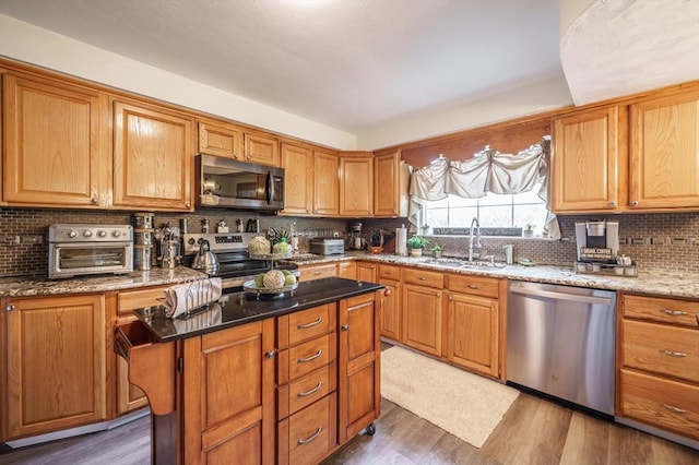 kitchen with stainless steel appliances, a sink, decorative backsplash, wood finished floors, and a center island