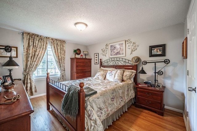 bedroom featuring light wood-style flooring, baseboards, and a textured ceiling