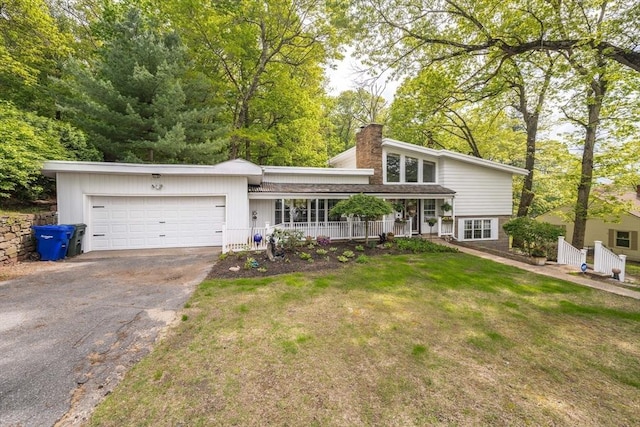 view of front facade with asphalt driveway, an attached garage, a chimney, a porch, and a front yard