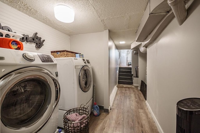 clothes washing area with wood finished floors, separate washer and dryer, baseboards, and a textured ceiling