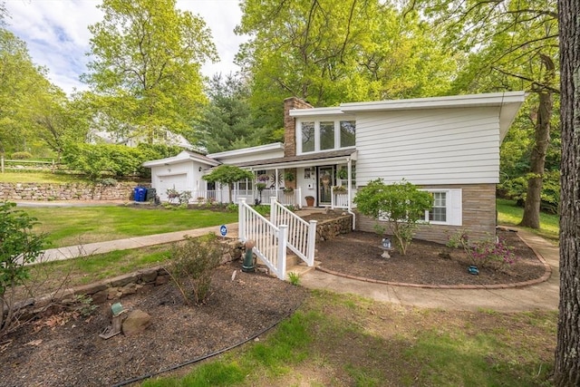 mid-century home featuring covered porch, an attached garage, a chimney, and a front yard