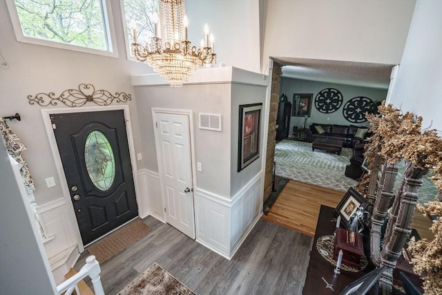 entrance foyer featuring a chandelier, wood finished floors, a wainscoted wall, a decorative wall, and a high ceiling