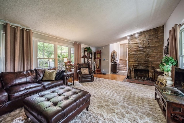 living room featuring a textured ceiling, vaulted ceiling, a fireplace, and wood finished floors
