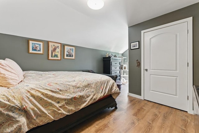 bedroom with baseboards, light wood finished floors, and vaulted ceiling