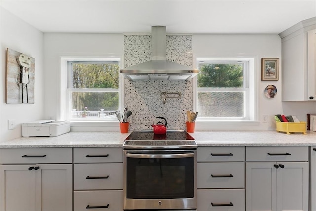 kitchen with gray cabinetry, a wealth of natural light, wall chimney exhaust hood, and stainless steel range with electric cooktop