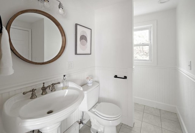 half bath with a sink, wainscoting, toilet, and tile patterned flooring