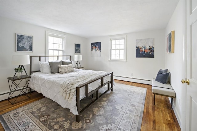 bedroom featuring a baseboard heating unit, multiple windows, wood finished floors, and baseboards