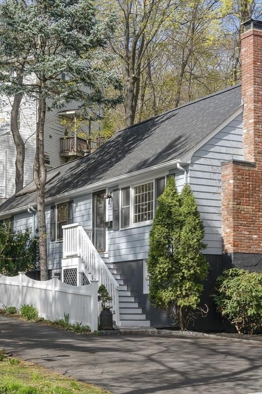 view of front of house featuring stairs, a chimney, fence, and roof with shingles