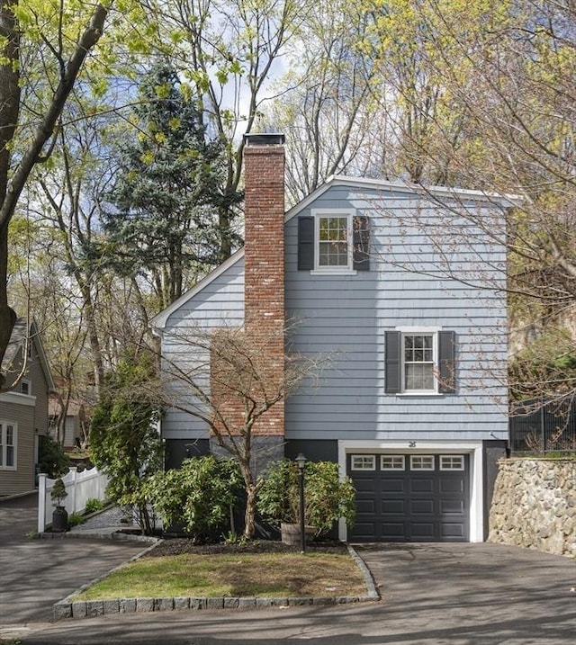 view of front of property featuring driveway, an attached garage, a chimney, and fence