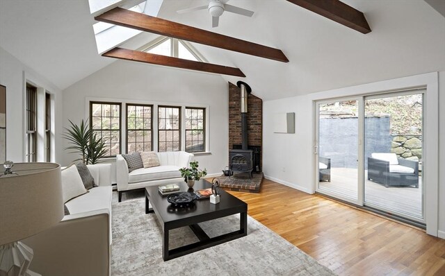 living area featuring a wood stove, beamed ceiling, light wood-type flooring, ceiling fan, and baseboards
