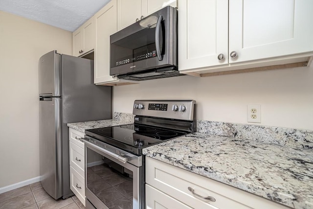 kitchen with light stone counters, a textured ceiling, appliances with stainless steel finishes, light tile patterned floors, and baseboards