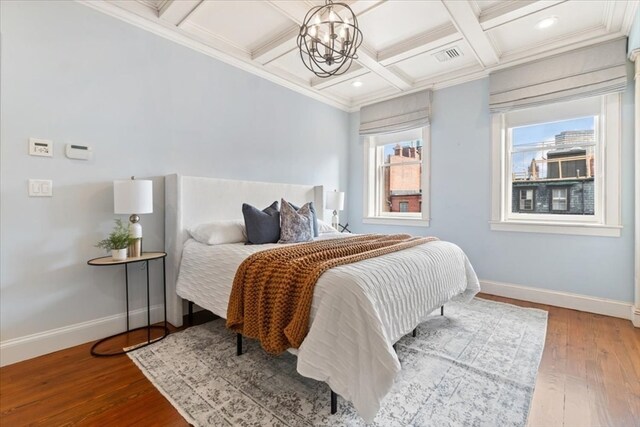 bedroom featuring wood-type flooring, ornamental molding, beamed ceiling, a notable chandelier, and coffered ceiling