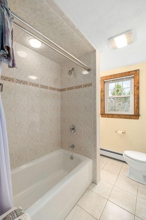 bathroom featuring shower / bathing tub combination, tile patterned flooring, toilet, and a baseboard heating unit