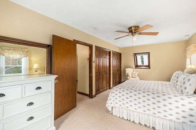 bedroom featuring a ceiling fan, multiple windows, light carpet, and two closets