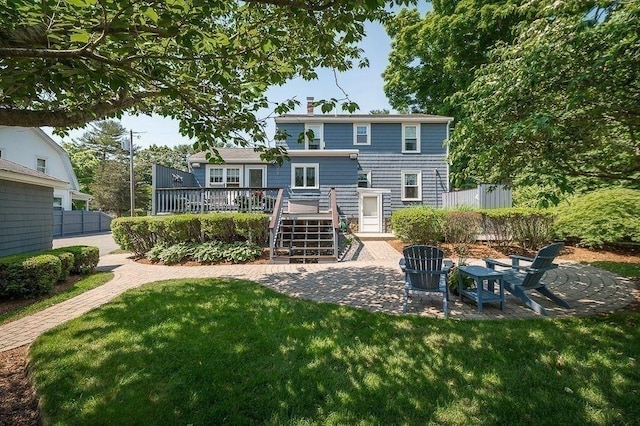 rear view of property featuring a patio, a chimney, a deck, a lawn, and fence