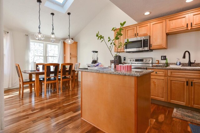 kitchen featuring stainless steel appliances, dark wood-type flooring, a kitchen island, a sink, and hanging light fixtures