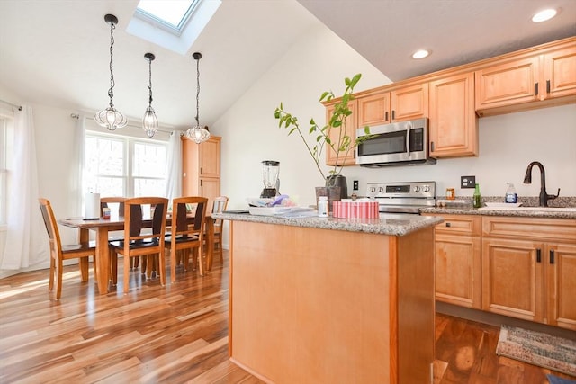 kitchen featuring lofted ceiling with skylight, appliances with stainless steel finishes, a center island, pendant lighting, and a sink