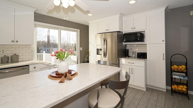 kitchen with stainless steel appliances, light stone countertops, white cabinets, and backsplash