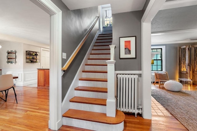 staircase featuring a wainscoted wall, radiator heating unit, wood finished floors, and a decorative wall